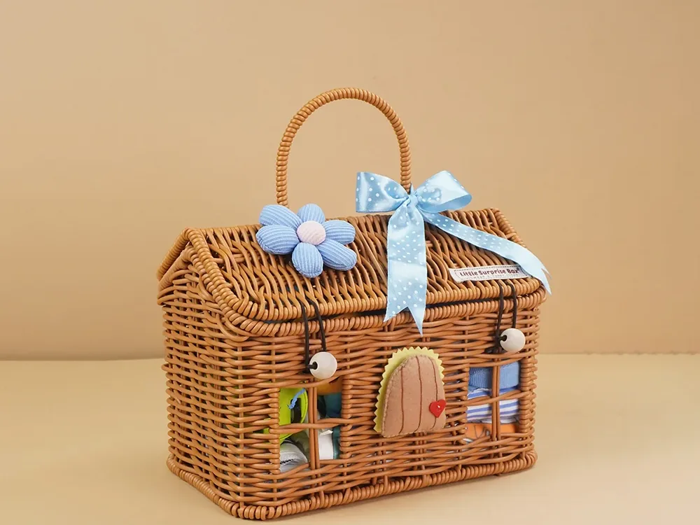 A wicker baby gift hamper shaped like a little house, tied with a blue ribbon