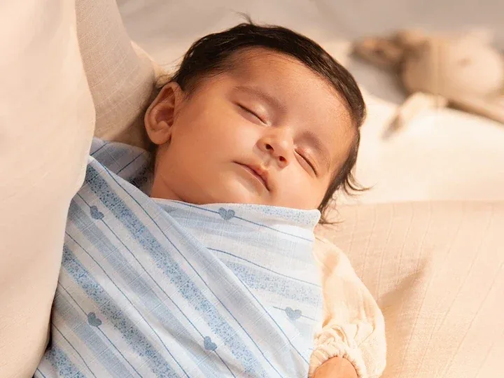 A sleeping newborn wrapped in a soft blue-striped muslin swaddle