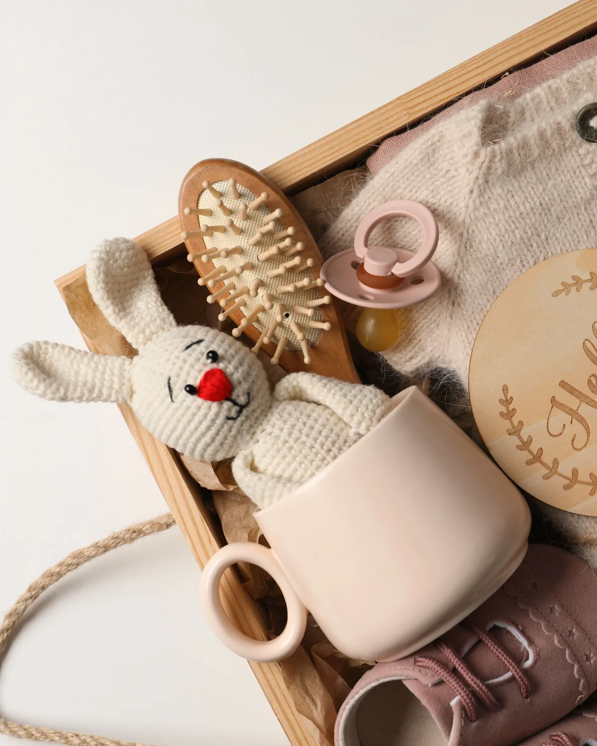 Wooden baby gift box holding a knitted bunny, a soft hairbrush, a pacifier, a ceramic mug and a wooden 'hello world' keepsake disc