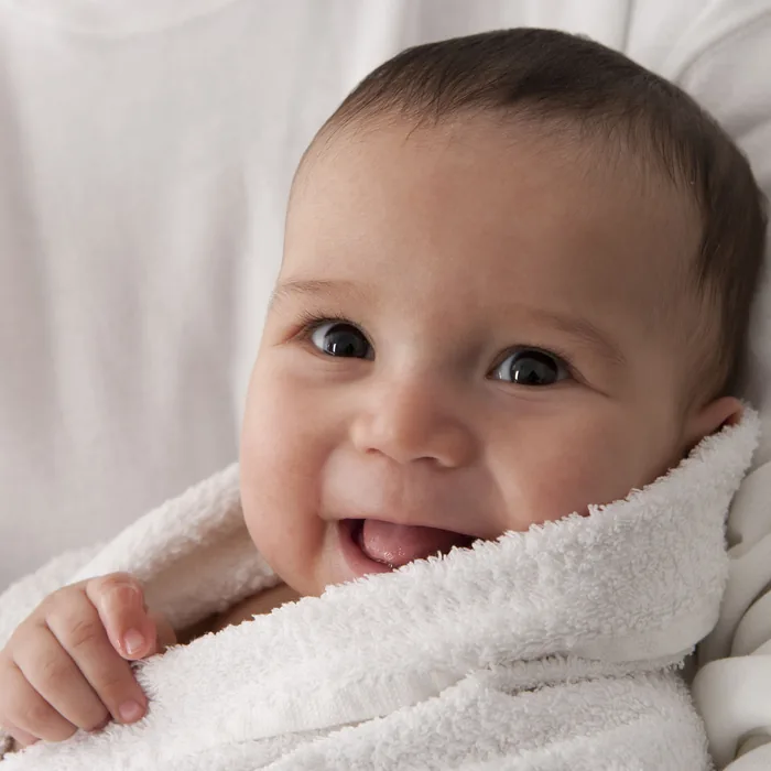 A smiling baby wrapped in a soft white towel
