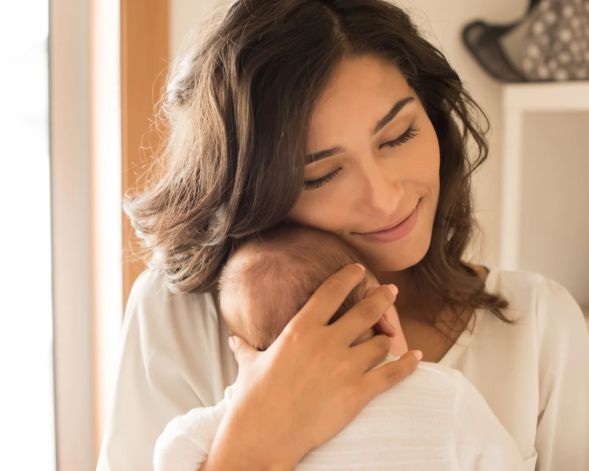 A mother cradling her sleeping newborn against her shoulder in soft natural light